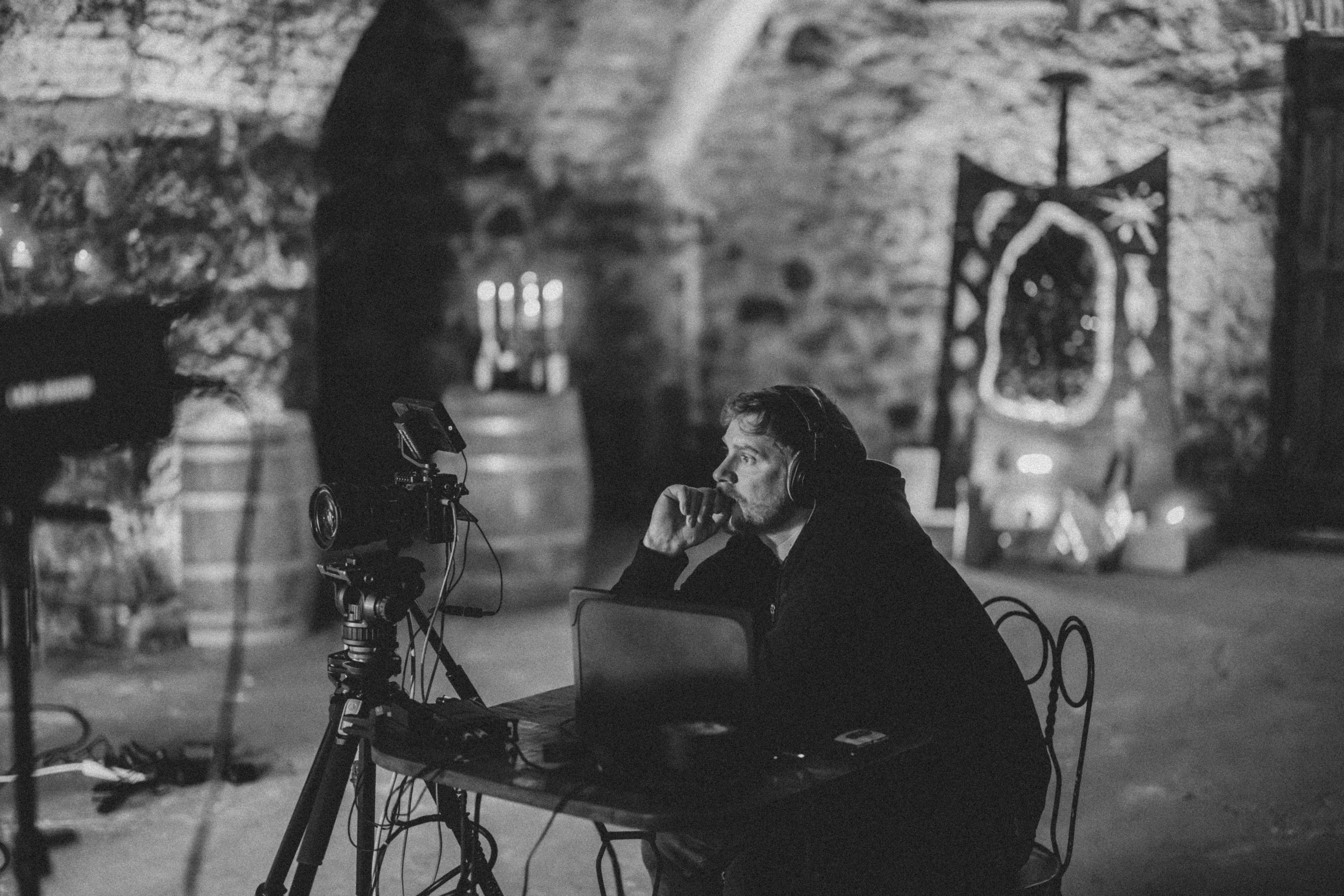 En blanco y negro, alguien habla por teléfono junto a un marco ornamentado con la cámara y las luces de rodaje al fondo
